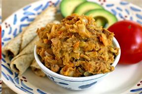 Refried beans in a boal with a tomato, avocado slides, and tortillas on the side.