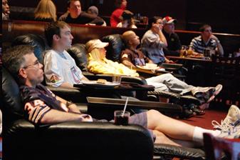 Group of adults in sports jerseys sitting in reclining chairs who appear to be watching a sporting event.